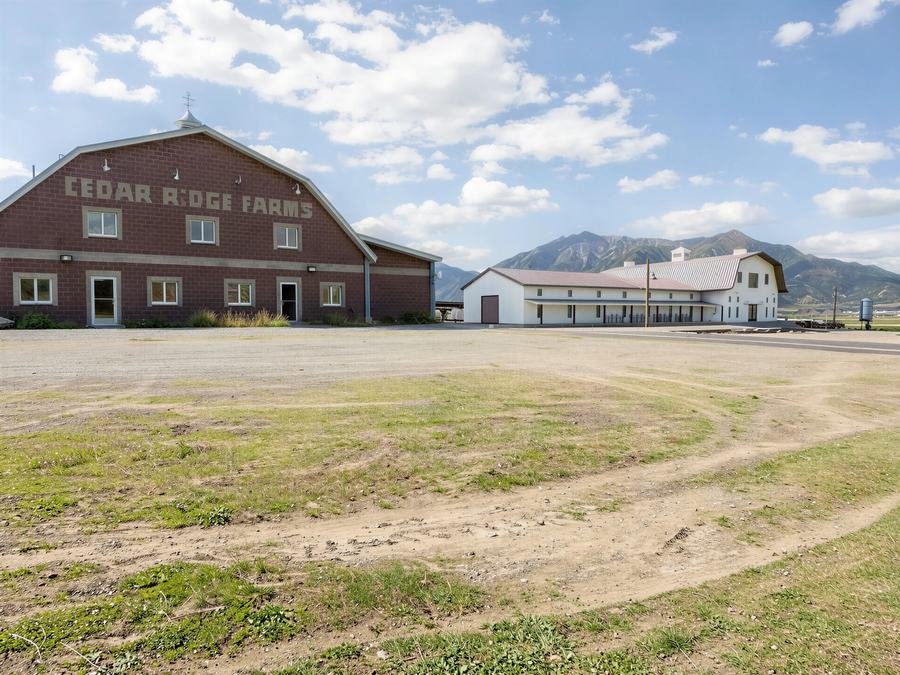 Rendering of a proposed white barn-style creamery and event building beside the existing brick Cedar Ridge Farms barn, with mountains in the background.